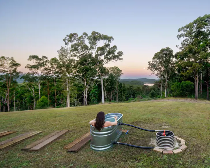 A woman sits in the outdoor bath gazing at the view at Lakeview Cottage Sunshine Coast Airbnb