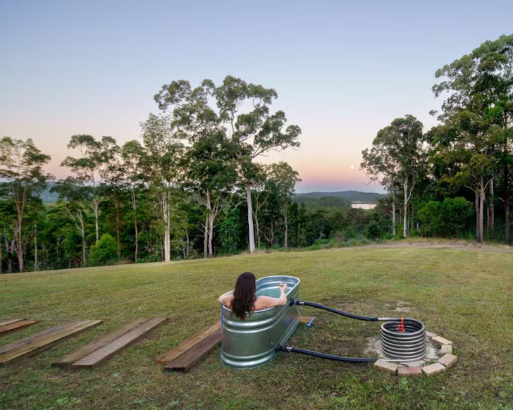 A woman sits in the outdoor bath gazing at the view at Lakeview Cottage Sunshine Coast Airbnb