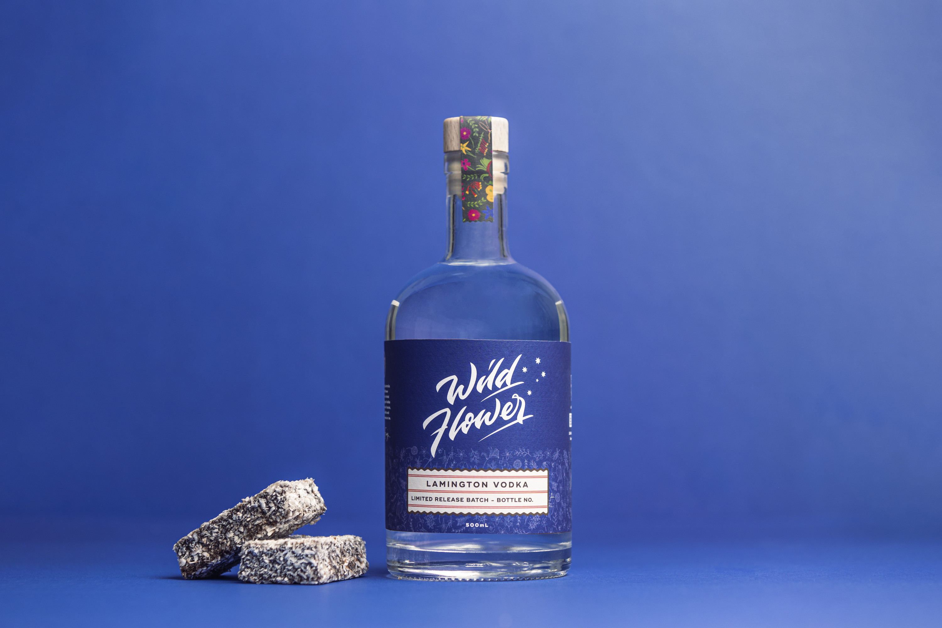a bottle of lamington-flavoured wildflower gin next to two lamingtons against a blue background