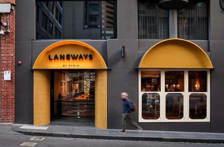 A person walks up a footpath, past  a yellow arched door way into Laneways By Ovolo, a pet-friendly accomodation in Melbourne.