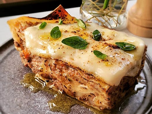 A piece of cheesy lasagna on a plate with basil on top. 
