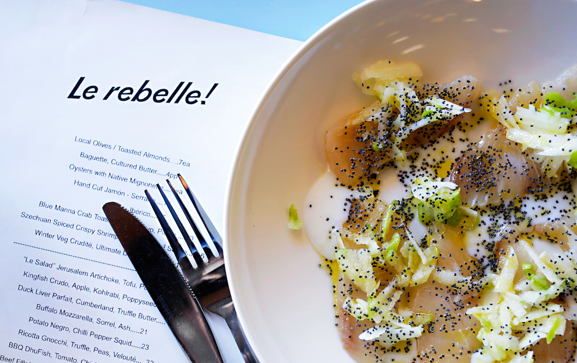 a close up of kingfish crudo dish on top of a menu from Le Rebelle