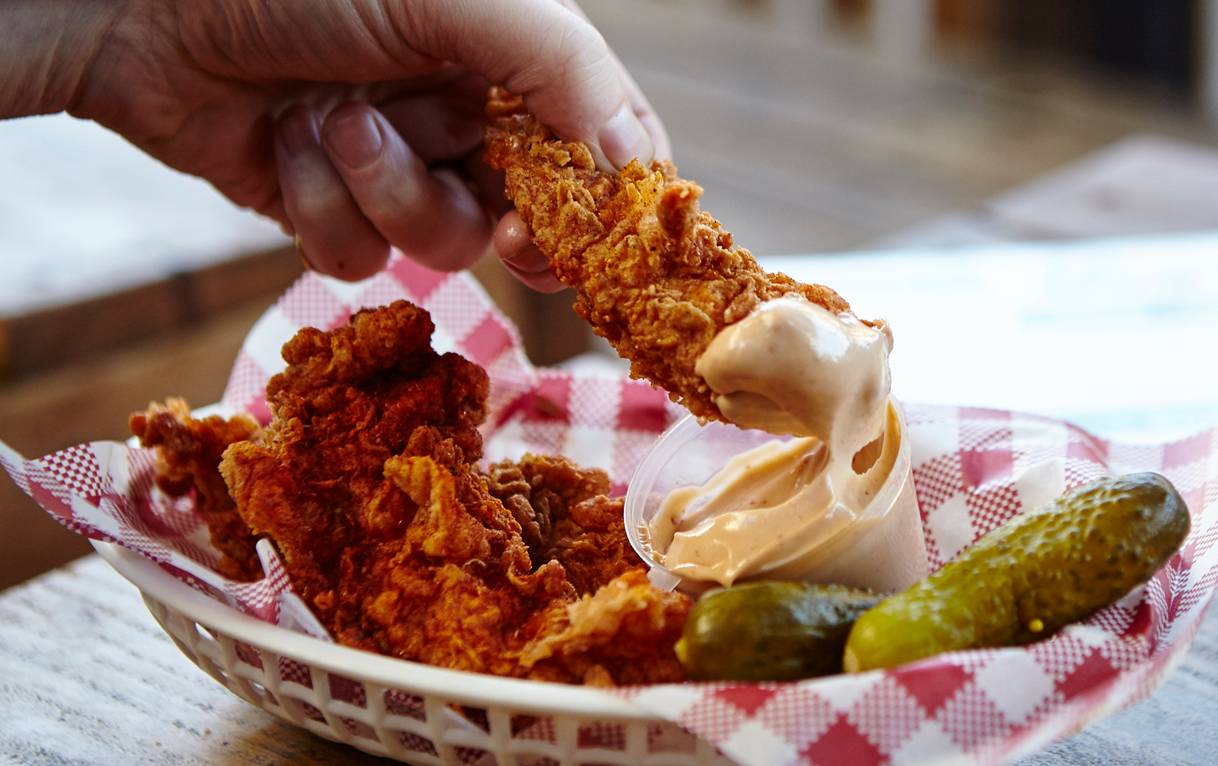 A person dipping a crunchy piece of the best fried chicken in Melbourne into a sauce. 