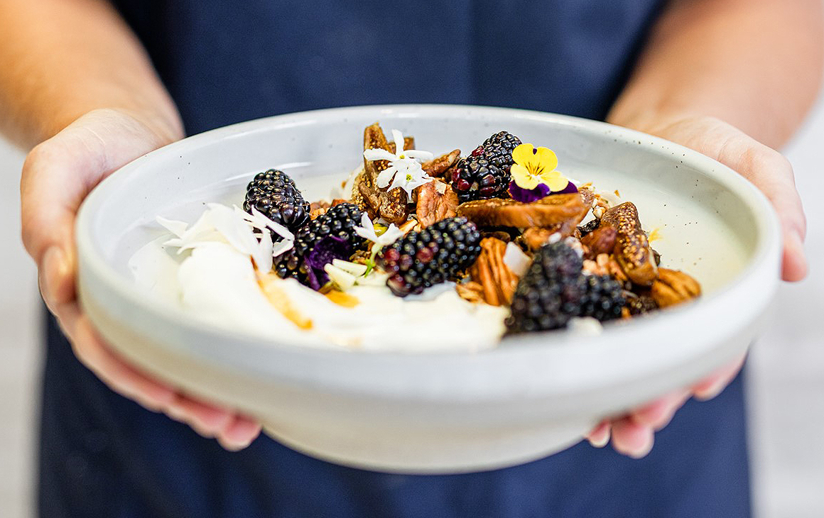 A person holds out a lovely looking dish of berries aloft at Lieutenant Coffee Bar & Eatery in Commercial Bay