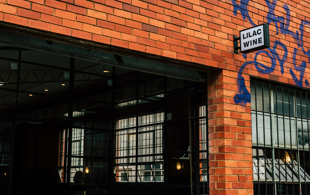 The outside of a brick building with a small black sign.