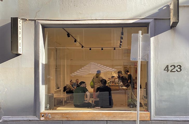 Two people sit within a cafe with a large window behind them at one of the best cafe Melbourne has to offer in 2024.
