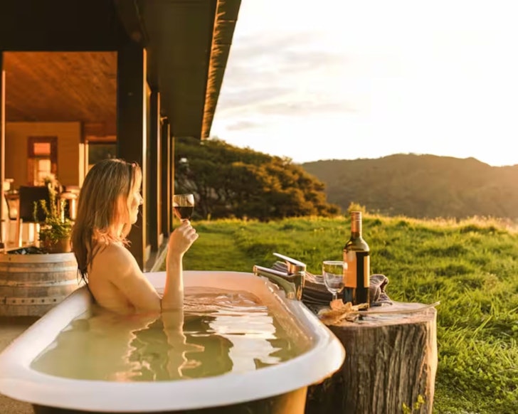 A woman sits in the outdoor bath at Little Greenie Ecohouse one of the best beach house Airbnbs in NZ