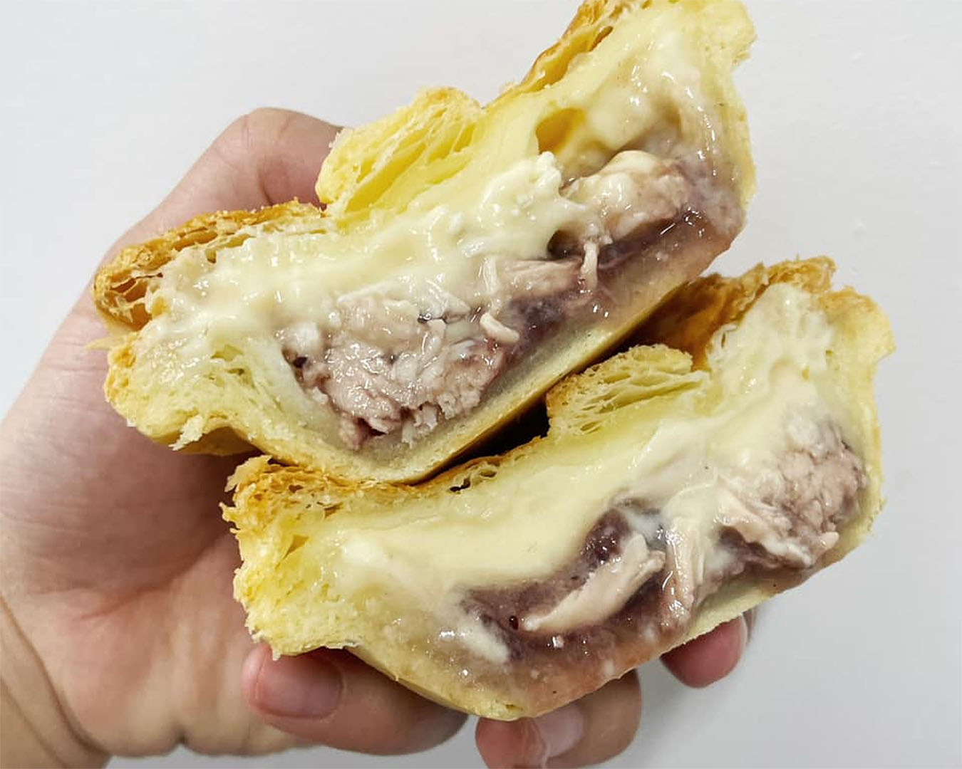 A hand holding a juicy chicken and cranberry pie, sliced in half from Loafer's Bakery, where you can get one of the best pies in Auckland. 