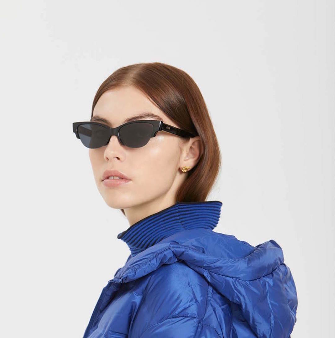 A woman wears a blue puffer jacket and sleek cateye sunglasses. 