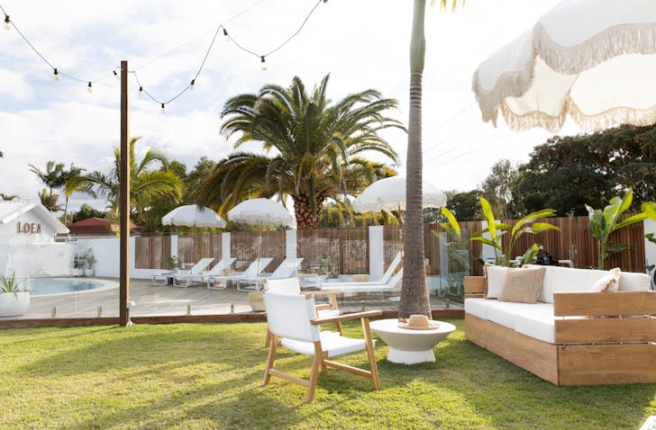 A garden decked out with festoon lights, palms and white furniture and beach umbrellas.