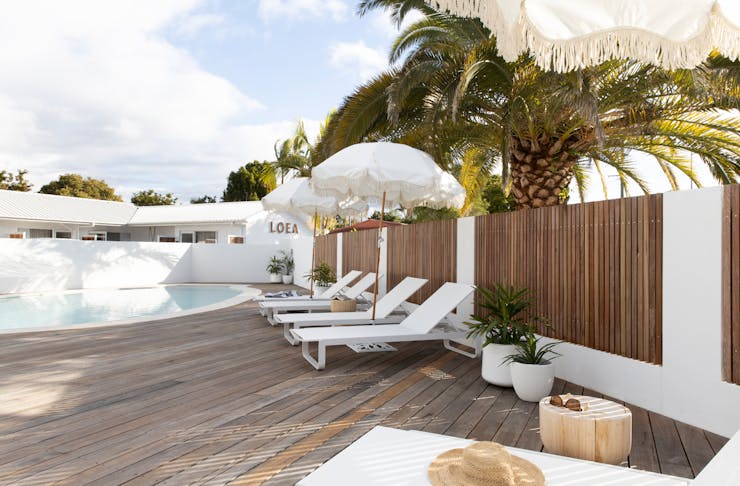 The pool area at LOEA Hotel, featuring sunbeams, white sun umbrellas and a timber deck.