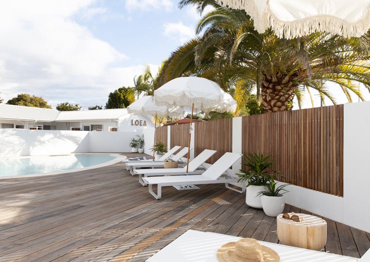 The pool area at LOEA Hotel, featuring sunbeams, white sun umbrellas and a timber deck.