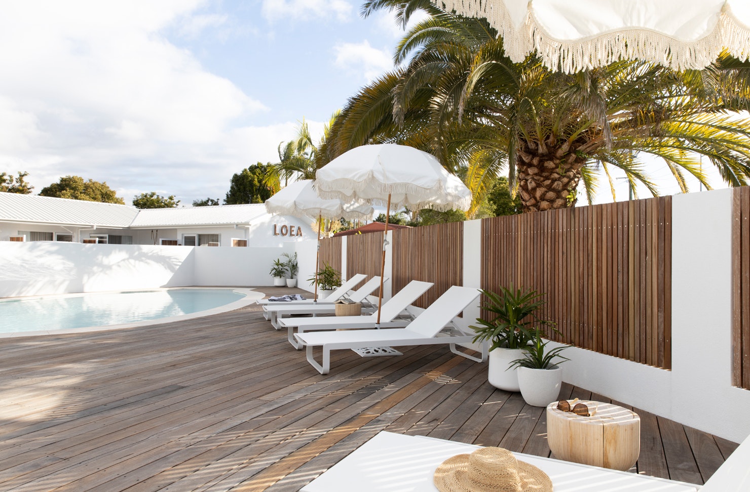 The pool area at LOEA Hotel, featuring sunbeams, white sun umbrellas and a timber deck.