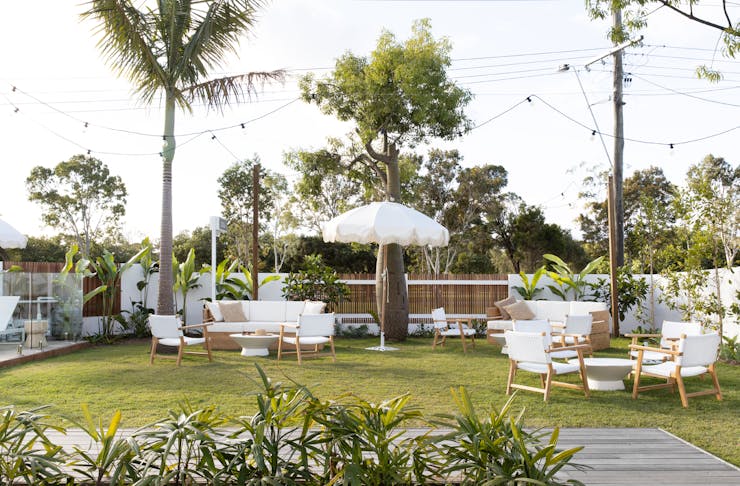 A garden decked out with festoon lights, palms and white furniture and beach umbrellas.