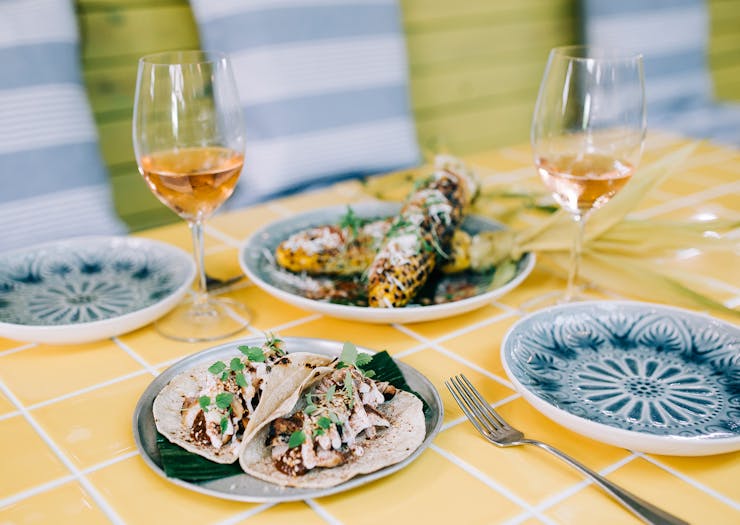 A yellow tiled table is filled with Mexican dishes and wine. 