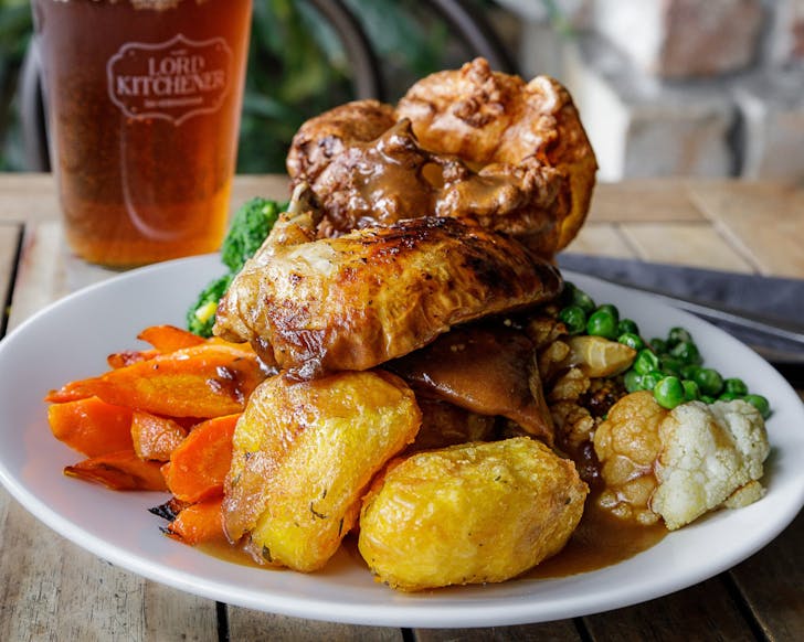 A plate is piled high with roasted vegetables and meat, infront of a glass of ice-cold beer.
