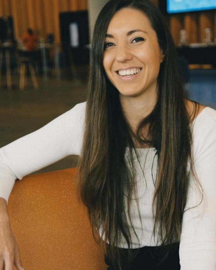 Lori Bahr sits on an orange chair looking happy. 