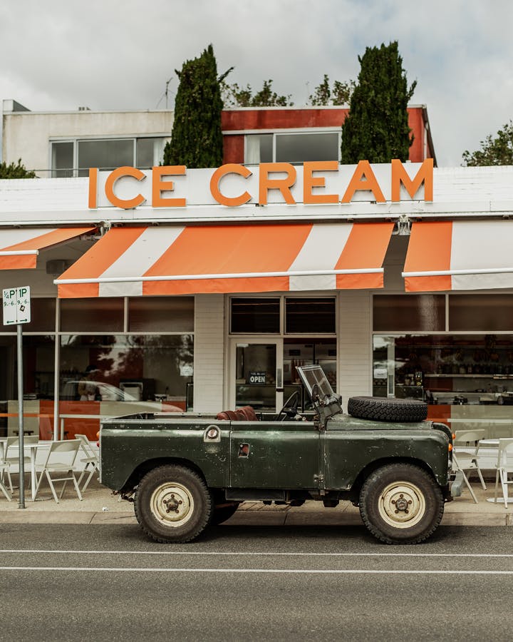 A orange and white-striped roof awning of a shop with a green jeep out front. 