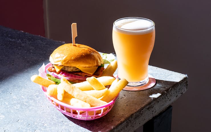 a burger and fries in a basket and a pint of golden beer