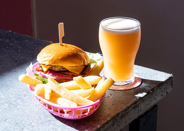 a burger and fries in a basket and a pint of golden beer