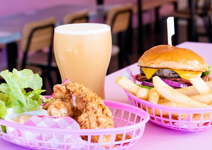a burger, fried chicken pieces and a pint of beer on a pink table