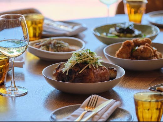 A table with various dishes and glasses with the focus on a plate of slow roasted pork shank.