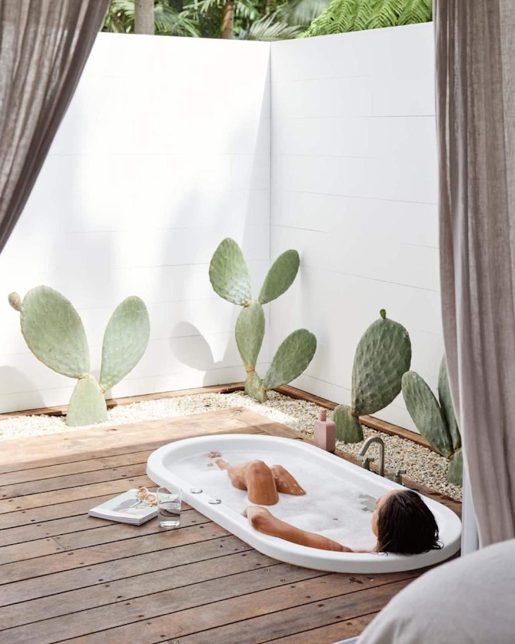 A woman relaxes in the outdoor bath on the deck surrounded by cactus plants at Luxe Cabin With Outdoor Spa near Brisbane Queensland