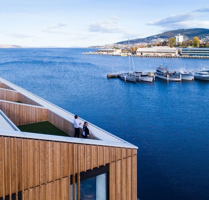 A couple stands on the balcony of the MACq 01 hotel one of the best in Tasmania looking out at boats on the water