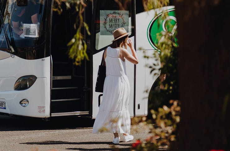 A woman in a white dress and a straw hat in front of the Merry Muster bus.