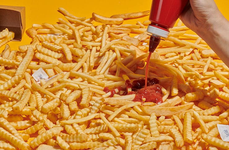 A table full of different cut hot chips with tomato sauce being poured over them. 