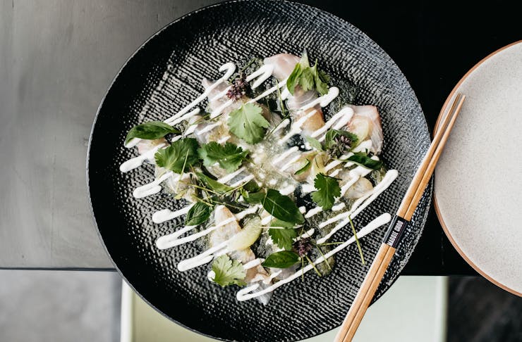An aerial shot of a plate of Kingfish sashimi drizzled in a white sauce.