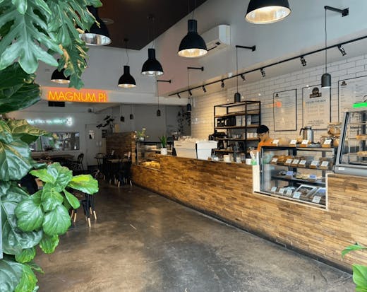 The inside of the store with plants and large wooden bar with a pie cabinet. 
