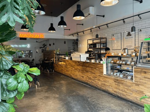 The inside of the store with plants and large wooden bar with a pie cabinet. 