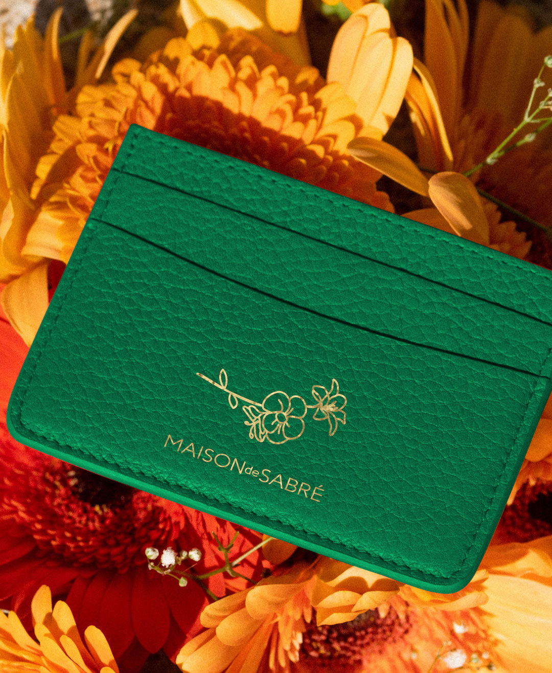 An emerald green cardholder lays on a bed of flowers. 