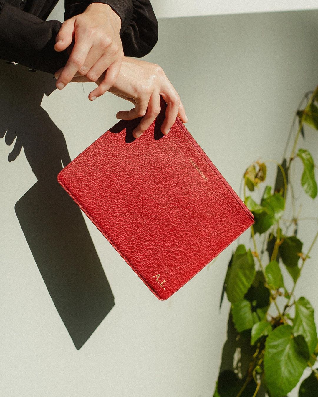 A woman holds are arms crossed with a red leather clutch. 