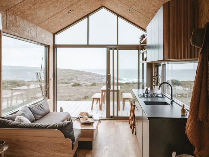 The interior of a cosy tiny home with views out to rugged coastline.