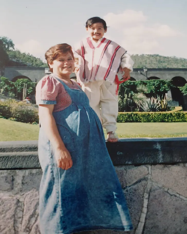 Mama Lety is pregnant and wears overalls, baby Jorge stands on a wall beside her wearing a poncho and a moustache he drew on.