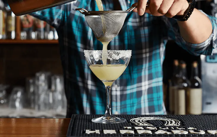 A person straining a Margarita into a glass. 