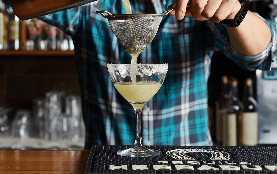 A person straining a Margarita into a glass. 