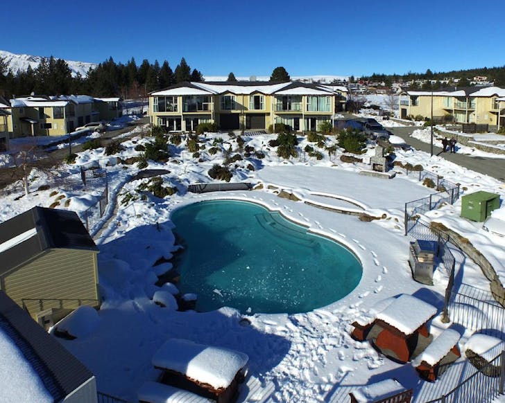 A resort with a large pool and spa pool with snowy mountain views. 