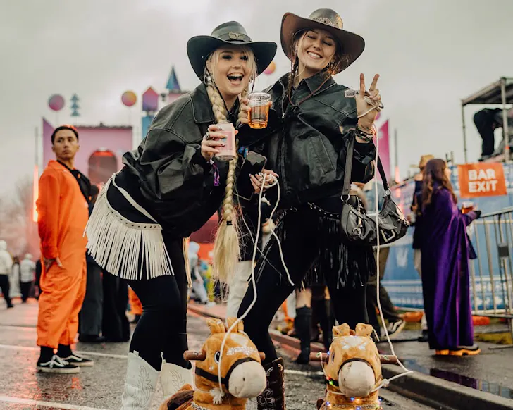 Two women dressed as cowboys with toy horses.