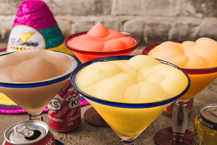 Four different coloured Margaritas with different soft drink cans around.