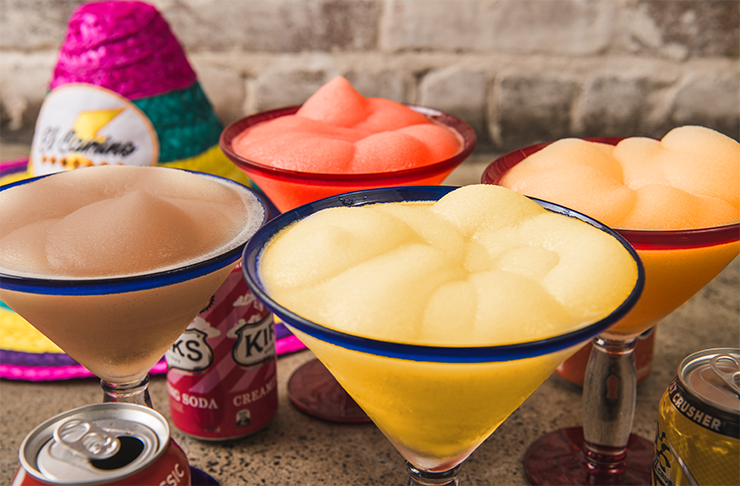 Four different coloured Margaritas with different soft drink cans around.