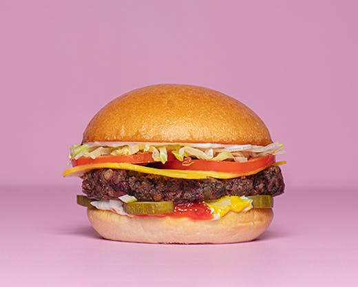A burger with cheese lettuce tomato and pickles against a pink backdrop