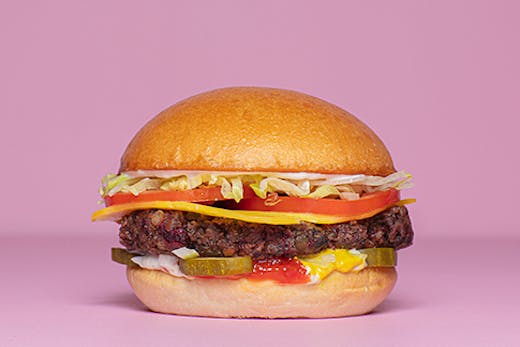 A burger with cheese lettuce tomato and pickles against a pink backdrop