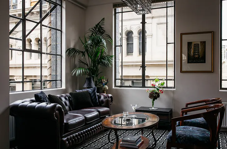 A chesterfield leather sofa sits in an art deco Airbnb Melbourne living room with a timber coffee table and two sitting chairs