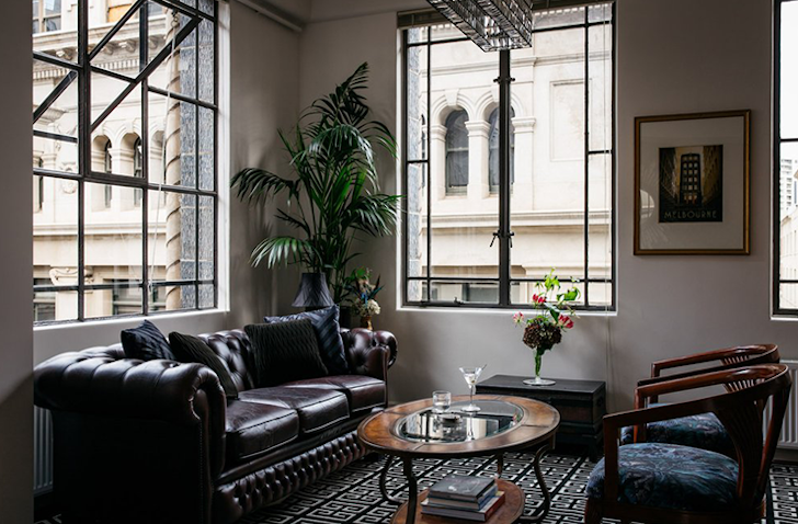 A chesterfield leather sofa sits in an art deco Airbnb Melbourne living room with a timber coffee table and two sitting chairs