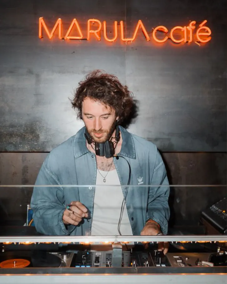 The DJ beneath a neon Marula Cafe sign in the underground basement club.