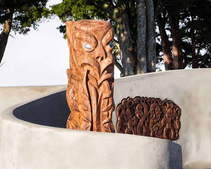 Two wooden Maori sculptures surrounded by a concrete semi-circle.
