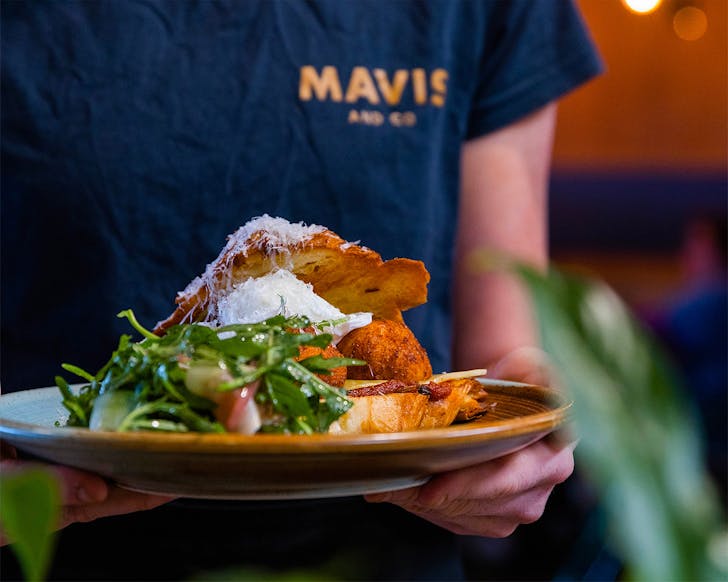 Someone brings a heaping plate of breakfast to the table at Mavis & Co, one of the best cafes in Hamilton.